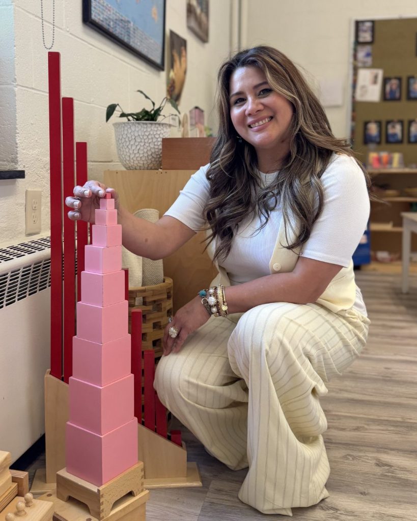 Founder Jouveth Shortell kneeling beside the Montessori Pink Tower in a SIMS classroom