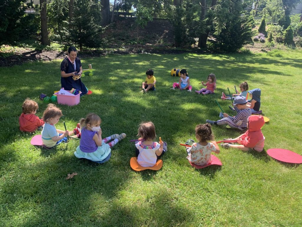 Children and their guide sitting in a circle on the grass during outdoor circle time at Spanish Immersion Montessori School