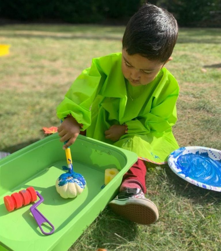 A child in a bright green smock paints at an outdoor table