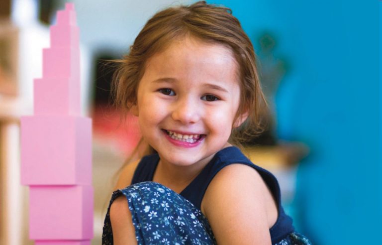 A smiling girl beside the Montessori Pink Tower