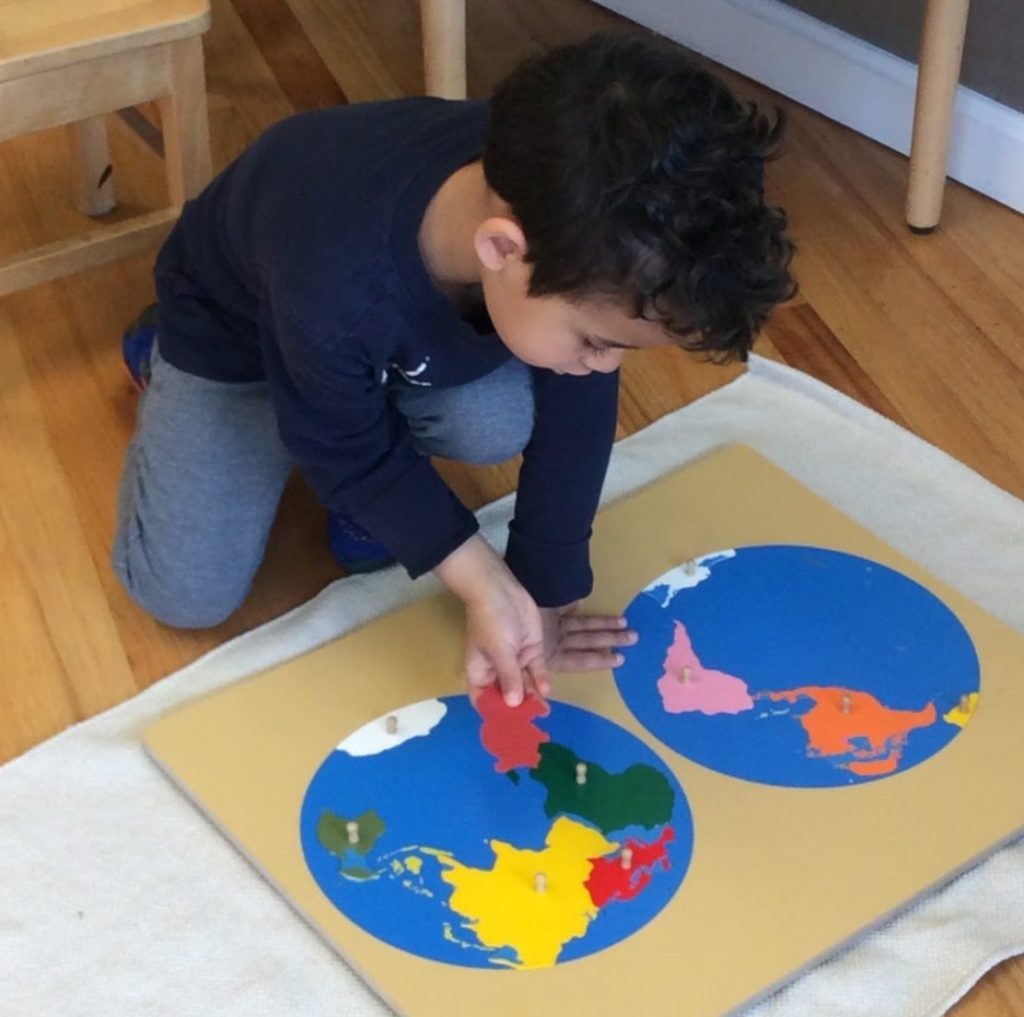 A child places continents into the Montessori puzzle map of the world
